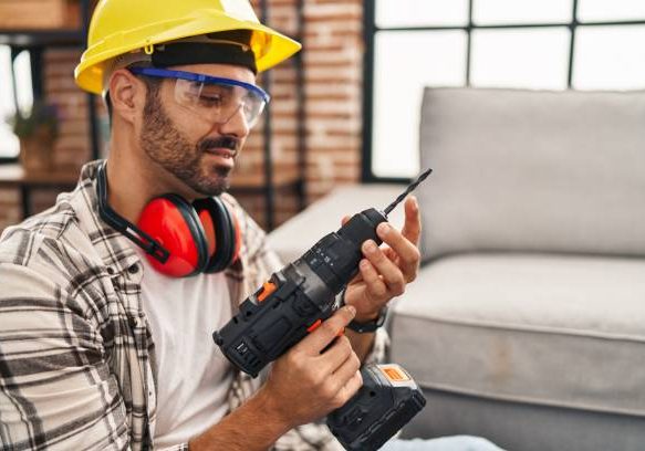 Young hispanic man worker smiling confident holding drill at home
